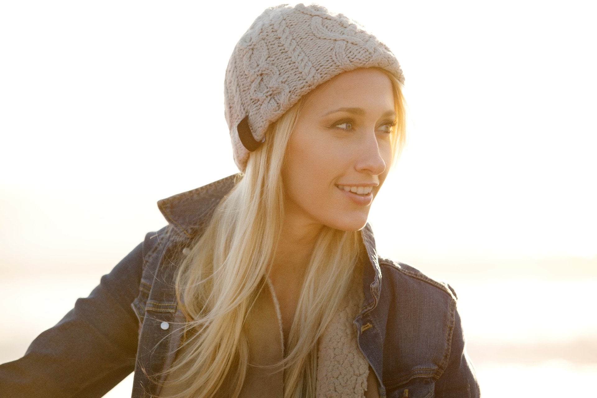 Lächelnde Frau mit gestrickter Mütze und Jeansjacke im warmen Sonnenlicht – stylische Accessoires bei Bella Vita – Mode & Lifestyle.