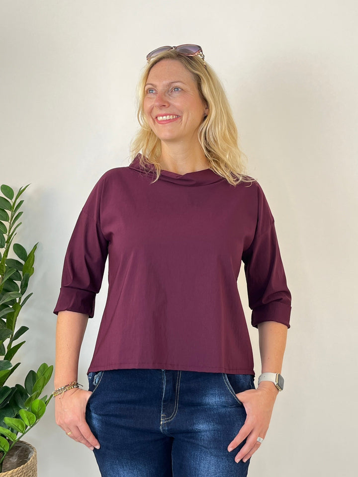 Bordeauxrotes Blusenshirt mit weitem Stehkragen und umgeschlagenen Ärmeln, getragen von einer Frau mit Jeans