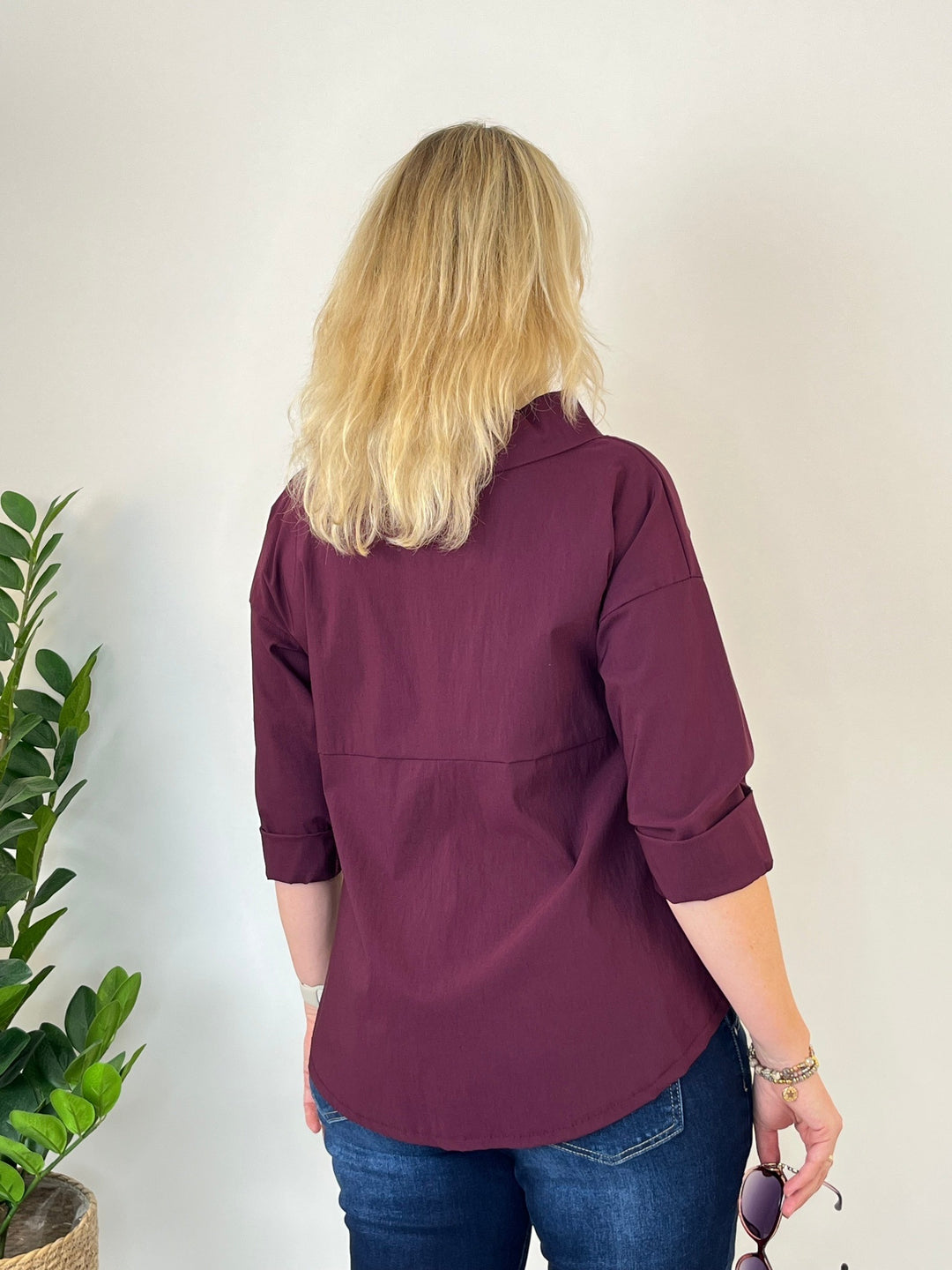 Rückansicht des bordeauxroten Blusenshirts mit lockerem Stehkragen und leicht gewölbtem Saum