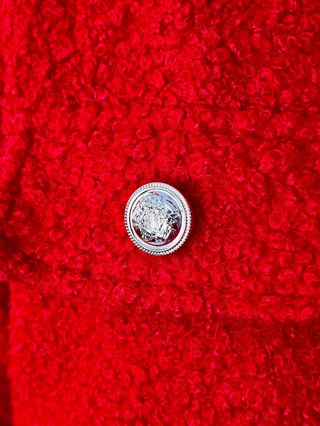 Nahaufnahme roter Bouclé-Stoff und glänzender silberner Schmuckknopf der Jacke