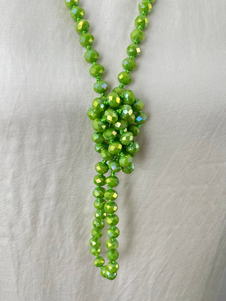 Detailaufnahme grüner facettierter Glassteine an Kette mit hängender Perlensträhne