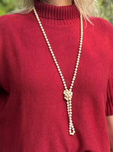 Beige Kette aus Glassteinen mit Knotendetail, getragen von Frau im roten Pullover