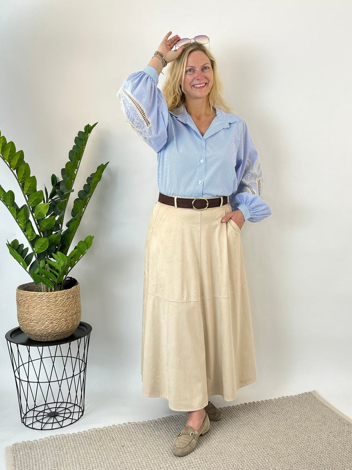 Woman styling beige faux suede skirt with striped blouse and sunglasses