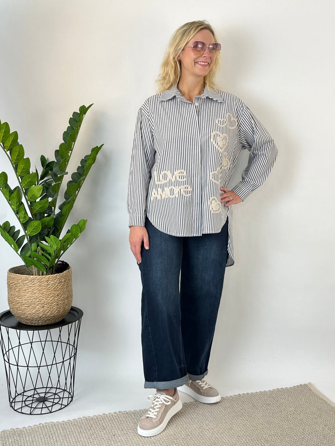 Frau trägt grau-weiße Longbluse mit Stickerei und Herzaufnähern im Streetstyle