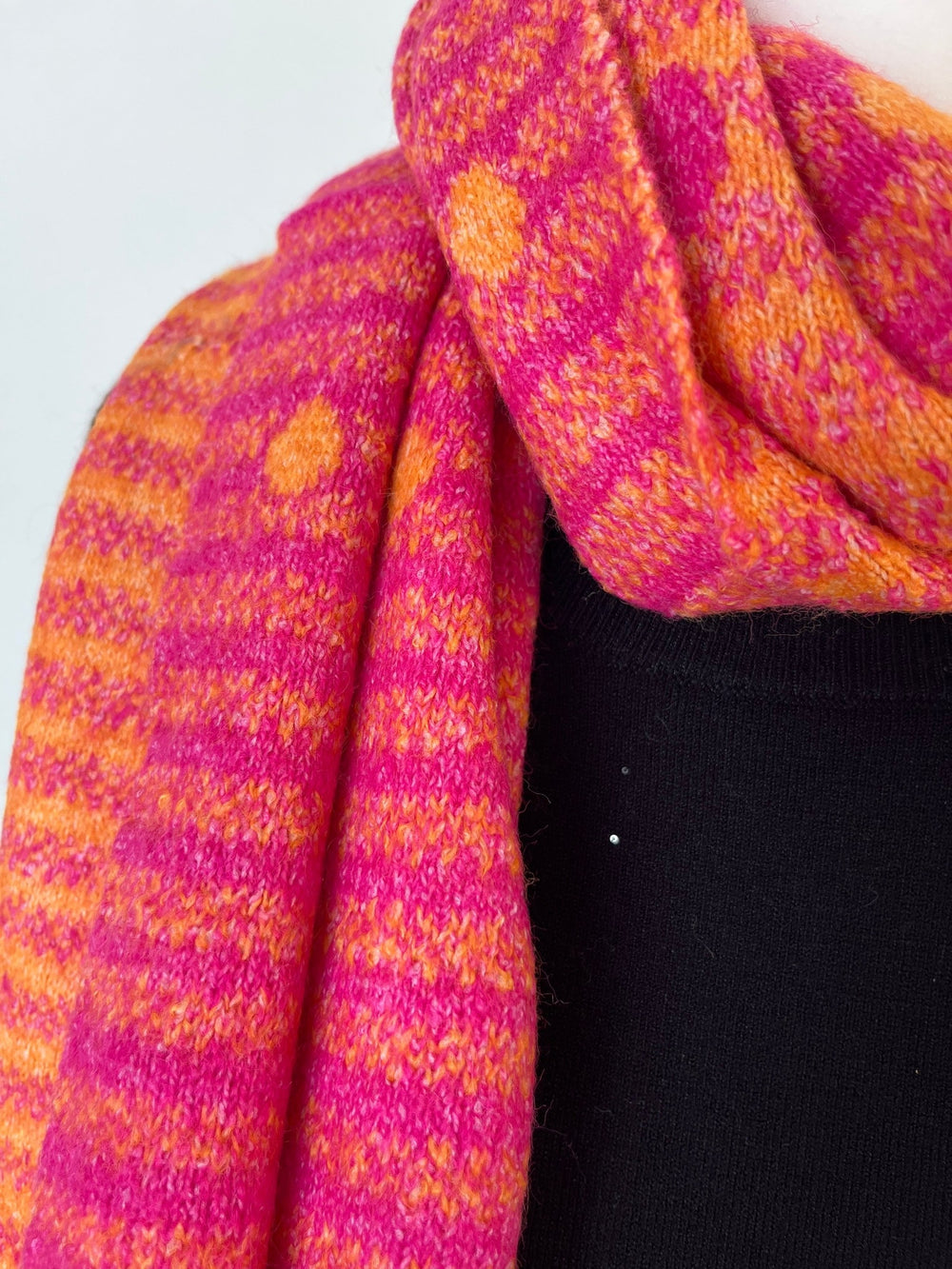 Pink-orangener Strickschal mit Streifen- und Punktmuster, getragen über schwarzem Oberteil