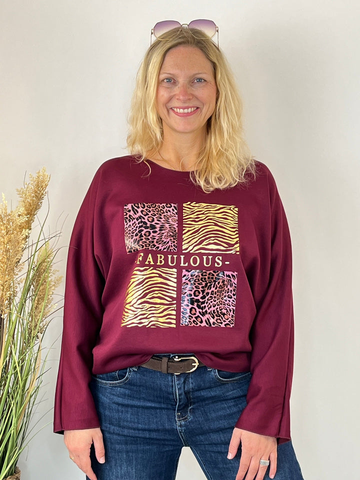 Breiter Ausschnitt des bordeauxroten Sweaters mit goldfarbenem Schriftzug
