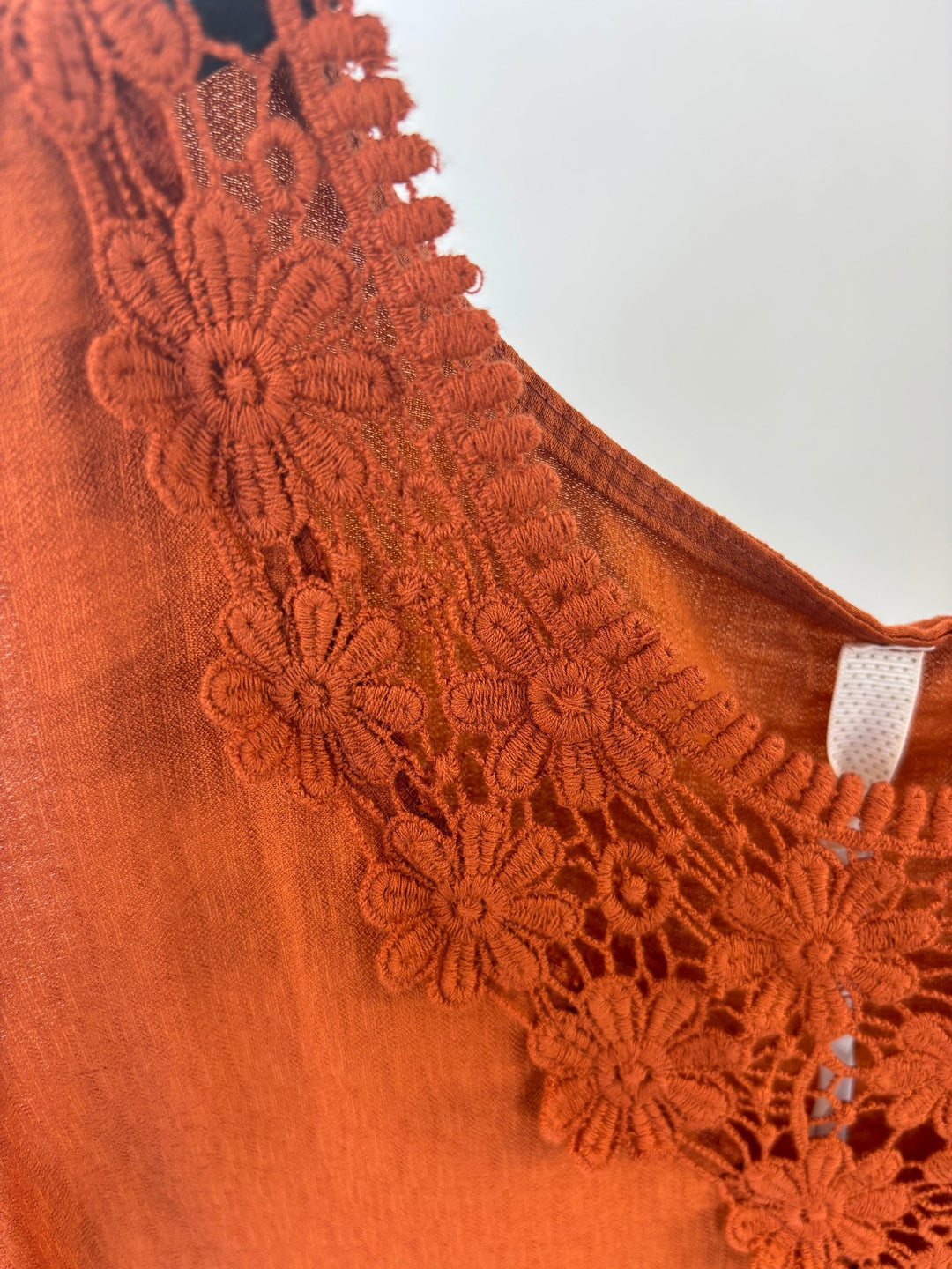 Detailaufnahme florale Spitze am V-Ausschnitt des orangefarbenen Tops